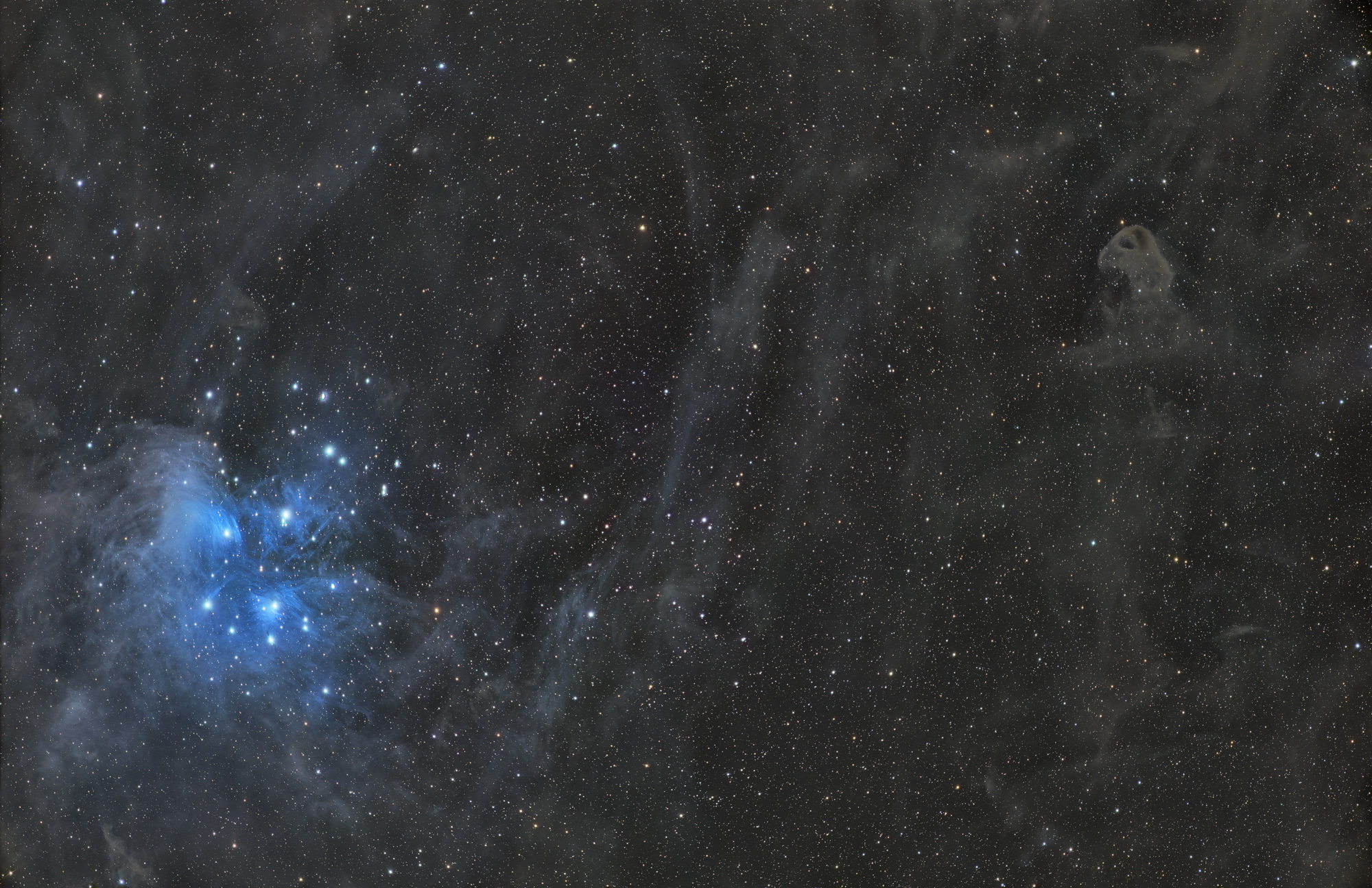 The open star cluster Messier 45 (Pleiades) is surrounded by bluish reflection nebulae and faint molecular clouds. The Baby Eagle Nebula LDN777 is visible in the upper right.